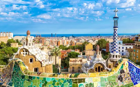 Kolorowe mozaiki i fantazyjne budowle Parku Güell, dzieło Antonio Gaudiego, na tle błękitnego nieba i Barcelony.