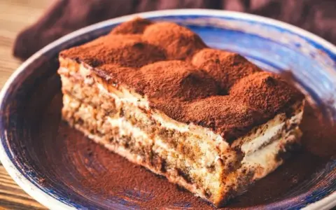 Pyszne tiramisu bez pieczenia, posypane obficie kakao, na niebieskim talerzu. Idealne na deser.