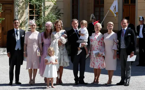 Familie in festlicher Kleidung, die überlegt, was anziehen zur Taufe. Ein Mann trägt ein Baby, Kinder und Frauen in eleganten Kleidern.