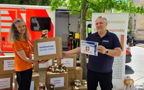 Zwei Personen vor einem Rettungswagen präsentieren Kartons für die Notfallseelsorge. Sie sind bereit, als Notfallseelsorger zu helfen.