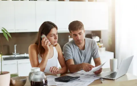 Para omawia finanse w kuchni. Kobieta rozmawia przez telefon, mężczyzna analizuje dokumenty. Temat: rozdzielność majątkowa a wspólny dom.