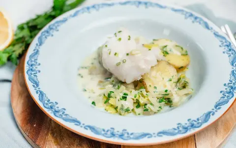 En vacker tallrik med pocherad fisk, potatis och vitkål i en krämig sås, garnerad med gräslök.