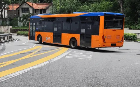 Pomarańczowo-niebieski autobus miejski na zakręcie drogi z żółtymi pasami.