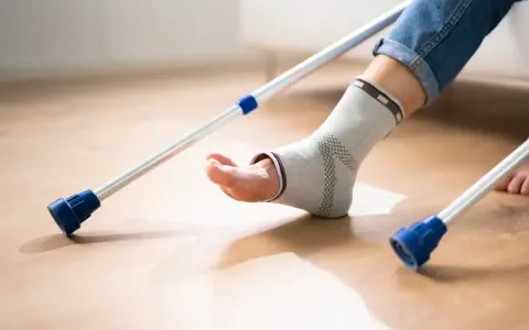 Osoba w opasce na kostce i jeansach próbuje chodzić po artrodezie stawu skokowego, wspierając się kulami.