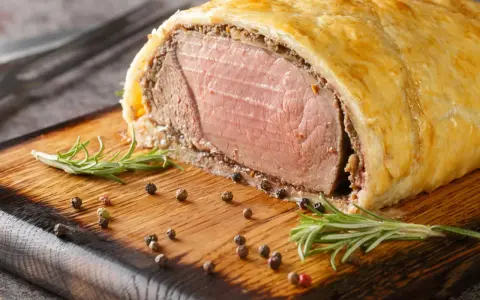 Wołowina Wellington na desce z rozmarynem i pieprzem.