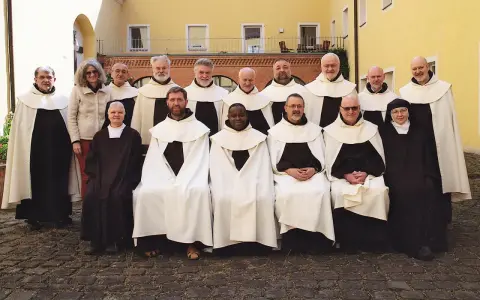 Gruppe von unbeschuhten Karmeliten in braunen Kutten und weißen Umhängen posiert vor einem gelben Gebäude.