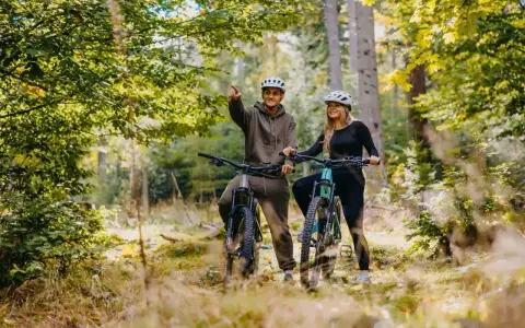 Para rowerzystów w kaskach na leśnej ścieżce. Mężczyzna wskazuje drogę, odkrywając piękną trasę w Szklarskiej Porębie.