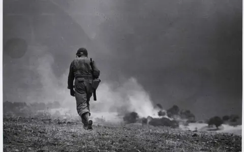 Soldato solitario cammina verso il fumo di battaglia, un'iconica immagine di Robert Capa.