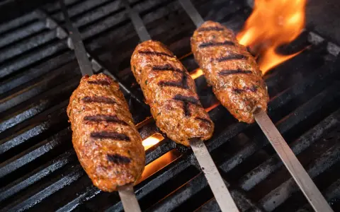 Drei saftige Seekh Kebabs brutzeln auf dem Grill über offenem Feuer.