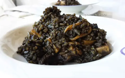 Un plato de arroz negro con trozos de calamar, servido en un cuenco blanco.