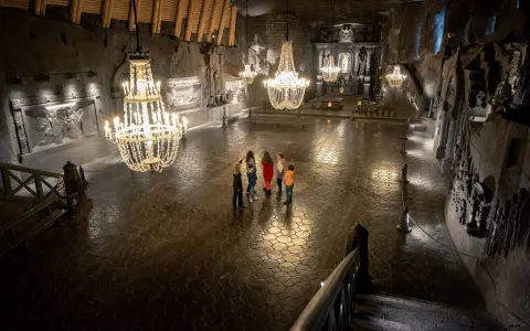Grupa turystów w podziemnej kaplicy Kopalni Soli w Wieliczce, oświetlonej kryształowymi żyrandolami.