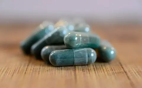 Pile di capsule verdi su un tavolo di legno. Si possono prendere due antibiotici insieme, ma sempre sotto controllo medico.