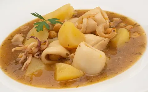 Guiso de garbanzos con trozos de calamar, patatas y perejil en un plato blanco.