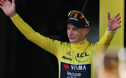 Radfahrer im gelben Trikot der Tour de France winkt jubelnd ins Publikum.