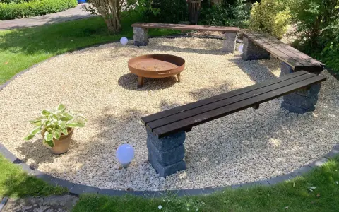 Gemütliche Sitzecke im Garten mit Kiesboden, Feuerstelle und Holzbänken. Perfekt für laue Sommerabende.