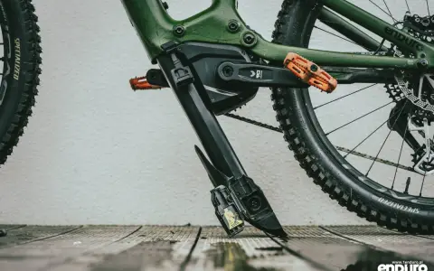 Zielony rower elektryczny z pomarańczowymi pedałami. Widoczny mechanizm, który ułatwia zrozumienie, jak wyjąć baterię z roweru elektrycznego.