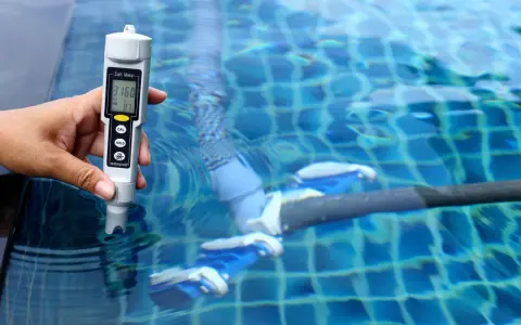 Mano mide salinidad de piscina con cloración salina. El medidor muestra 3160 ppm, indicando posibles problemas.