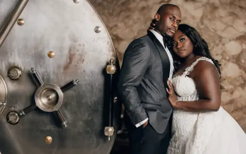 A groom in a patterned tuxedo jacket stands beside a vintage vault door. The father of the bride wears a sharp, dark suit with a satin lapel.