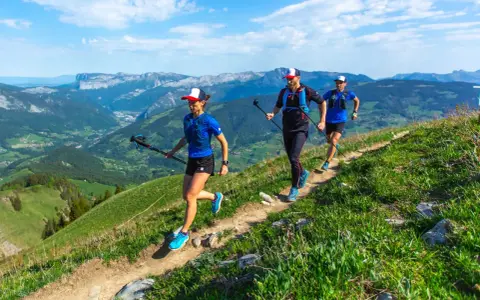 Trzy osoby uprawiające speed hiking na górskim szlaku, ciesząc się pięknymi widokami.