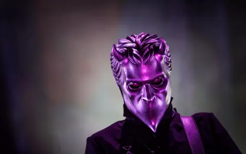 En av Ghost medlemmar utan mask, med en metallisk lila mask som täcker ansiktet.