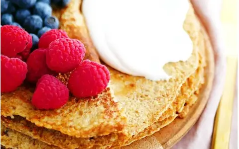 En hög med nyttiga pannkakor toppas med grädde, hallon och blåbär. En perfekt frukost eller mellanmål.