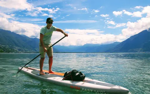 Mann auf SUP-Board mit Paddel, genießt die Geschwindigkeit auf dem See vor einer Bergkulisse.