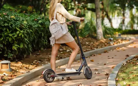 Ragazza su monopattino elettrico in un parco autunnale. Ricorda l'obbligo casco monopattino per la tua sicurezza.