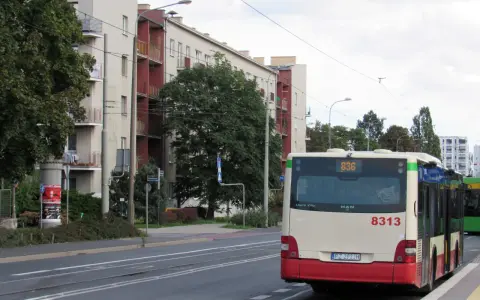 Autobus 8313 z numerem linii 836 czeka na przystanku. W tle budynki mieszkalne i drzewa.