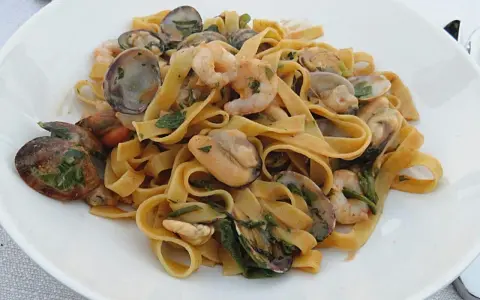Un piatto invitante di tagliatella di mare con gamberi, cozze e vongole, condita con erbe fresche.