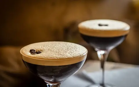 Dwa drinki z pianką i ziarnami kawy. Wybór między Espresso Martini a Irish Coffee.