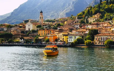 Un giallo battello solca il lago, dirigendosi verso il pittoresco borgo di Limone sul Garda, con le sue case colorate aggrappate alla montagna.