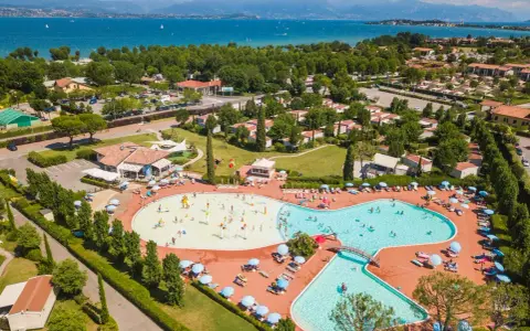 Widok z lotu ptaka na kompleks basenów i domków kempingowych w Sirmione. Woda lśni w słońcu, a ludzie cieszą się wakacjami na łonie natury.