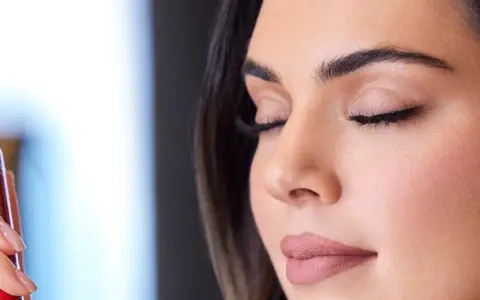 Una mano sostiene un spray fijador de maquillaje rojo. Ideal para cuando usar y mantener tu look perfecto.