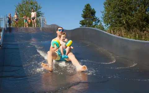 Vater und Sohn rutschen lachend die Wasserrutsche im Bostalsee Strandbad hinunter.