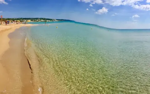 Spiaggia delle Maldive in Puglia: sabbia dorata, acque cristalline e un cielo azzurro con nuvole bianche. Un paradiso terrestre.