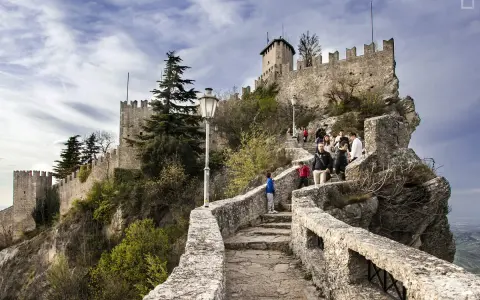 Sentiero roccioso verso le torri di San Marino, un viaggio nella storia. Turisti salgono la scalinata che porta alle antiche fortificazioni.