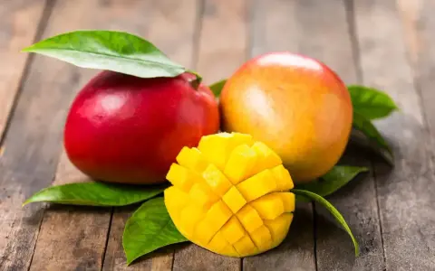 Dwa soczyste mango, jedno czerwone, drugie pomarańczowe, i jedno pokrojone w kostkę, idealne, gdy jest sezon na mango.