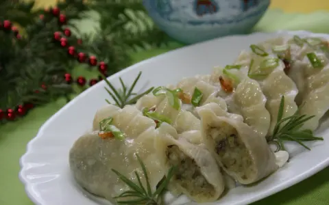 Pyszne pierogi ukraińskie, udekorowane szczypiorkiem i rozmarynem, prezentują się apetycznie na białym talerzu.