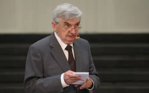 Starszy mężczyzna w garniturze, który prowadzi jeden z dziesięciu, trzyma kartkę.