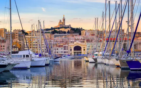 Barche a vela ormeggiate nel porto di Marsiglia, con la Basilica di Notre-Dame de la Garde sullo sfondo. Un'ottima vista per chi cerca cosa vedere a Marsiglia vicino al porto.