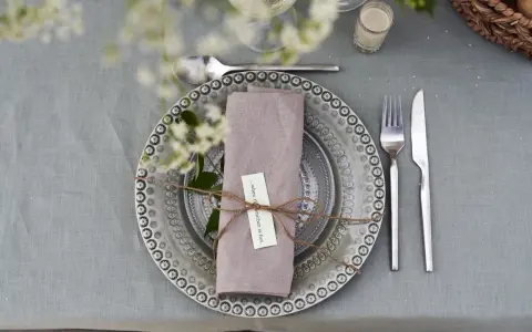 Vacker dukning med linneservetter, blommor och en korg med bröd. Perfekt för en sommarfest.
