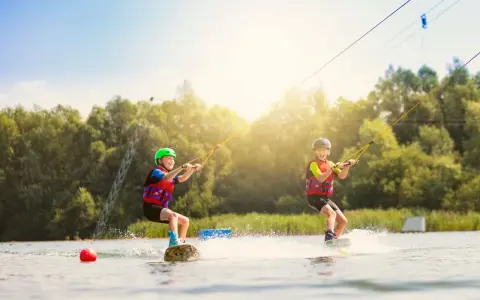 Zwei Kinder üben Wakeboarden am Nesthauser See, gezogen von einer Seilbahn.