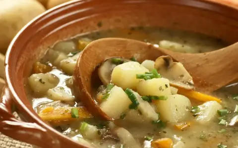 Zupa ziemniaczana przepis babci. Aromatyczna, sycąca zupa z ziemniaków, marchewki i grzybów, podana w glinianej misce z drewnianą łyżką.