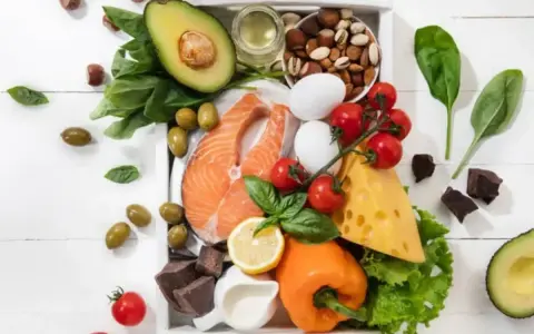 Składniki na dieta keto jadłospis: łosoś, awokado, jajka, ser, orzechy, oliwki, warzywa i gorzka czekolada.