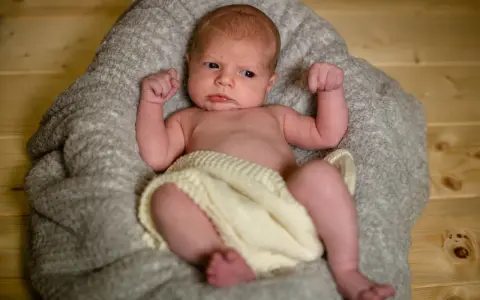 Un neonato con un'espressione curiosa, avvolto in una coperta, pronto per un servizio fotografico flash neonati.