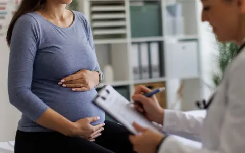 Visita medica: una donna incinta tiene la pancia mentre il medico annota sul foglio, forse il tracciato delle contrazioni preparatorie.