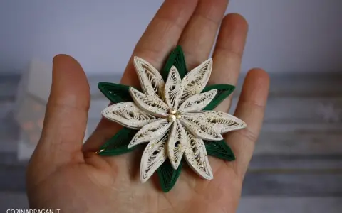 Un fiore di carta in quilling, perfetto per un tutorial di quilling natale. Dettagli dorati e petali bianchi e verdi.