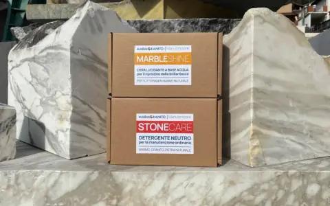 Due scatole di prodotti per la pulizia del marmo, "Marble Shine" e "Stone Care", appoggiate su blocchi di marmo grezzo.