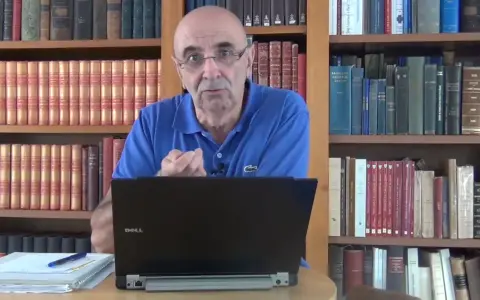 Un homme parle devant un ordinateur portable, entouré de rayonnages remplis de livres anciens, rappelant les archives départementales 85.