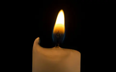 Jasny płomień świecy na czarnym tle. Jego migotanie symbolizuje nadzieję i przemijanie, a jego znaczenie jest głębokie.